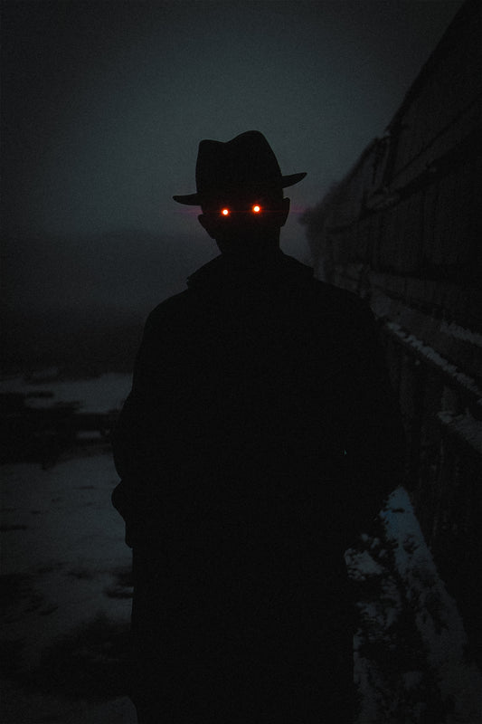 Frostbound Sentinel - the Hat Man, a shadow figure with glowing red eyes standing in the snow beside a train